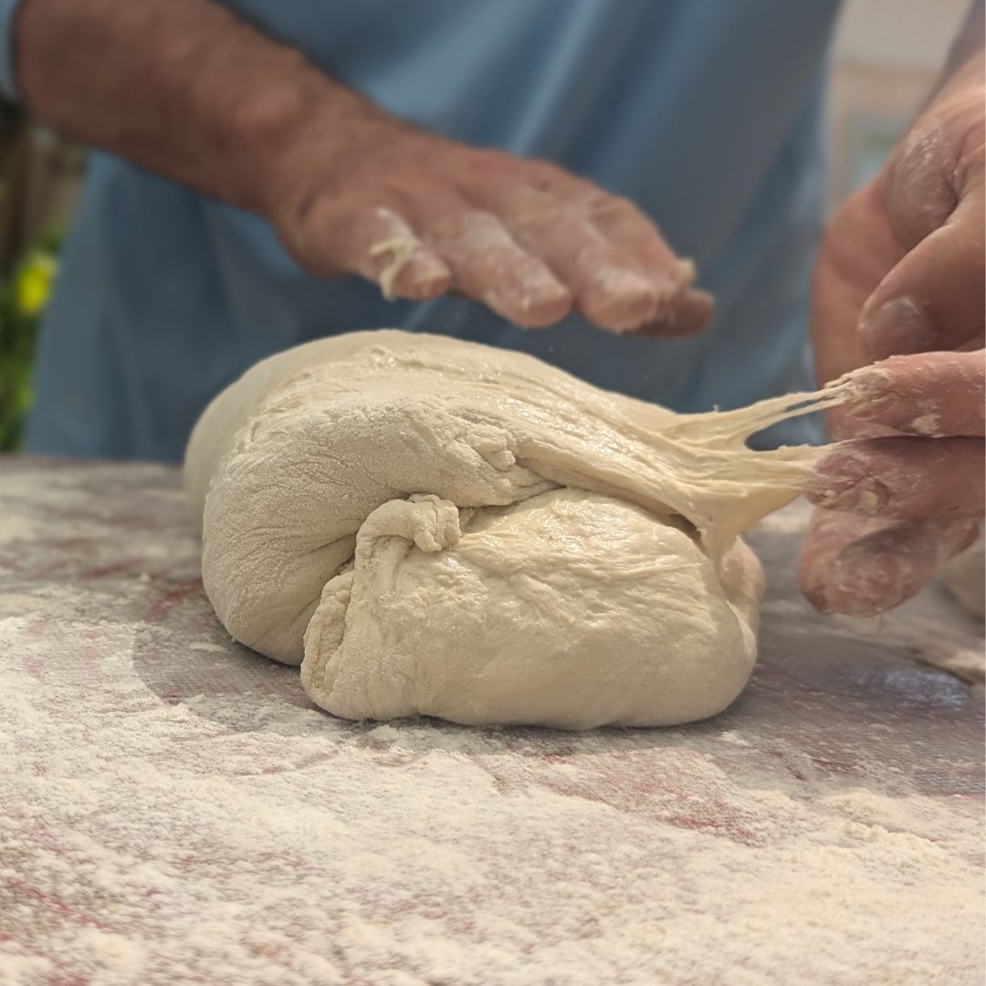 Hands mixing sourdough dough in a bowl, building gluten structure