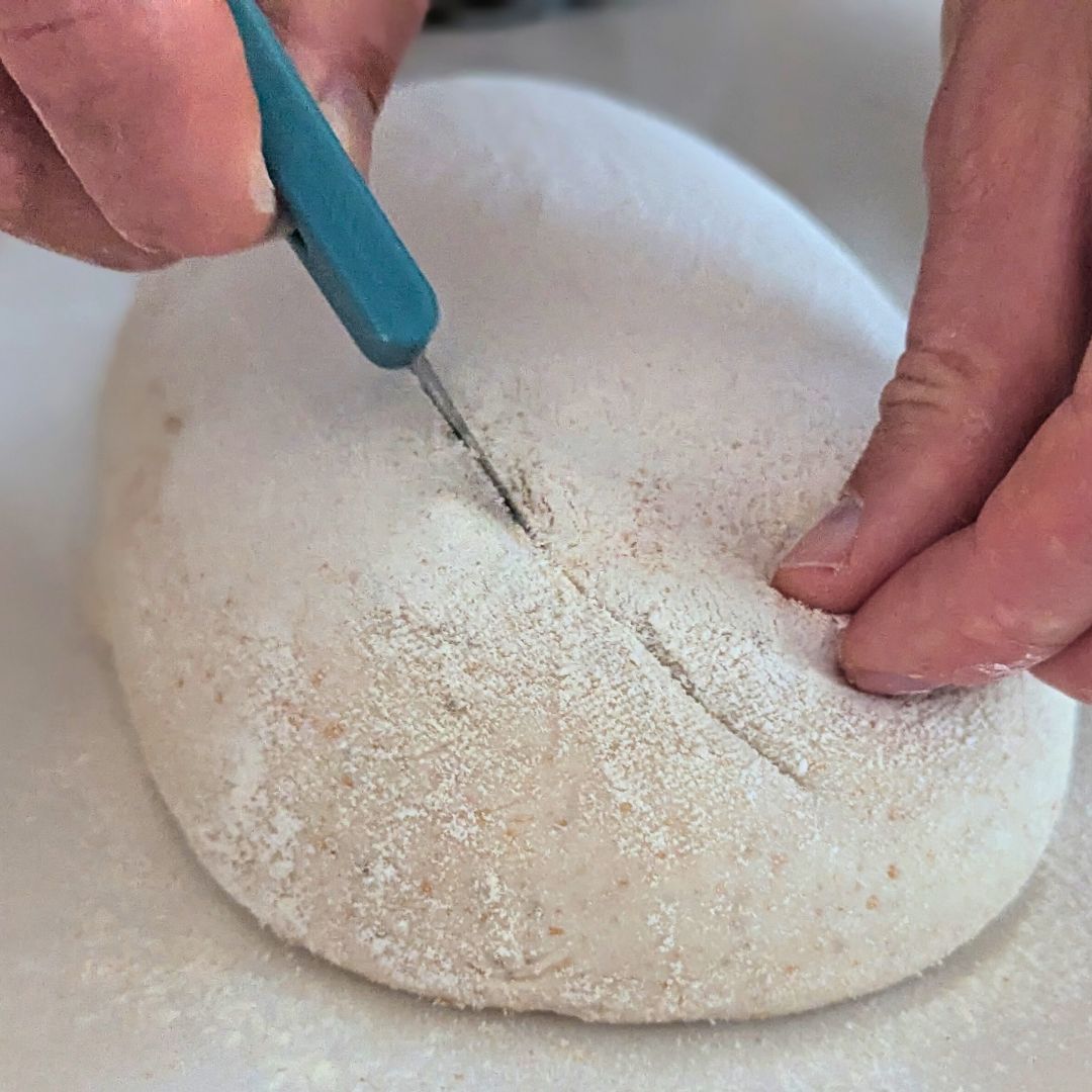 Close-up of sourdough being scored with a bread lame before baking.