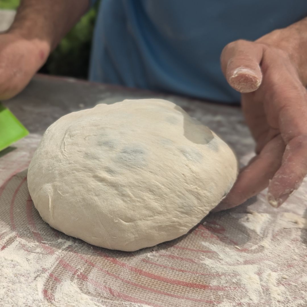 Hands shaping sourdough dough into a round boule on a floured surface